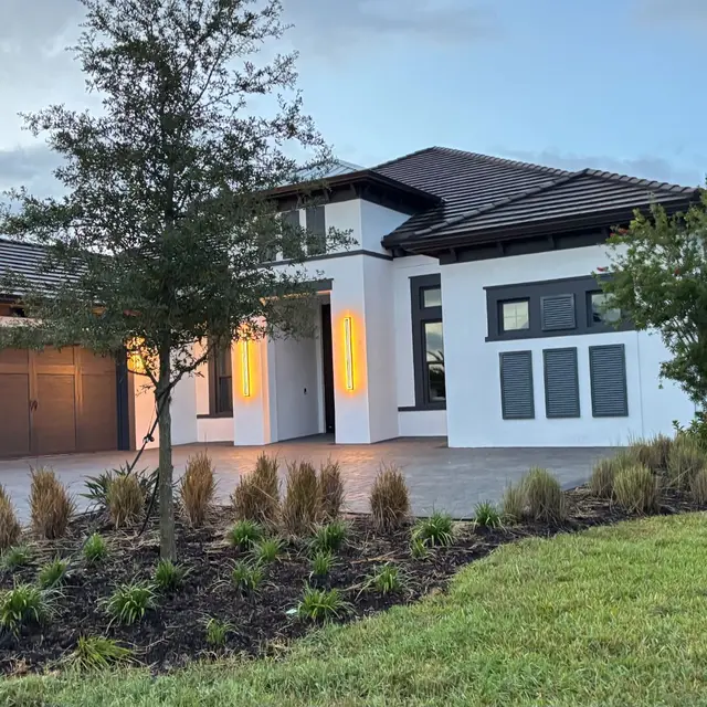 Modern white home with dark roof and landscaped front yard at dusk