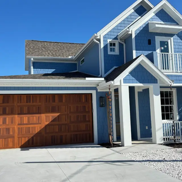 Blue two-story home with white trim and a stained wood garage door