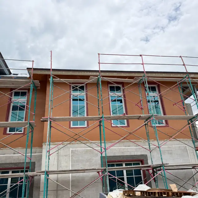 Two-story stucco home under scaffolding during exterior painting