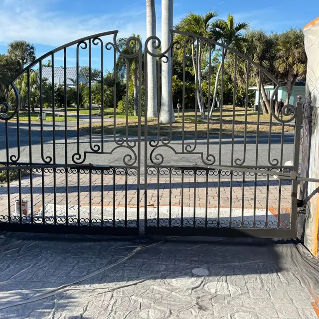 Wrought-iron driveway gate painted black with the stone pillars masked off
