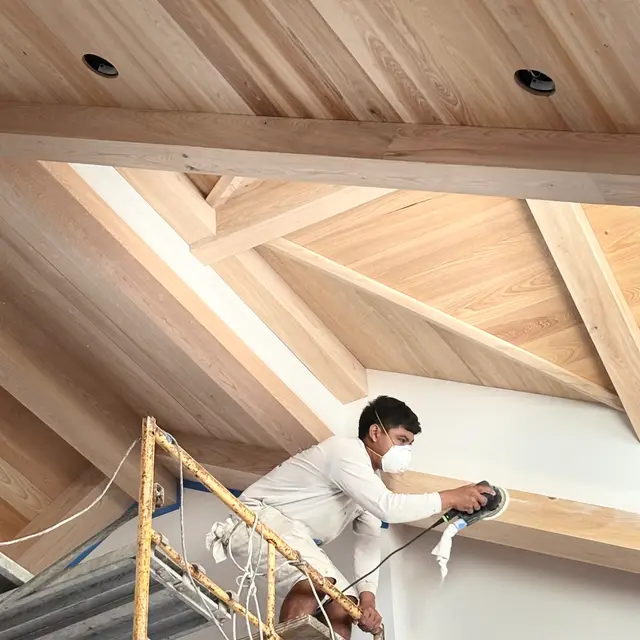 Painter on scaffolding spraying a vaulted wood ceiling and beams