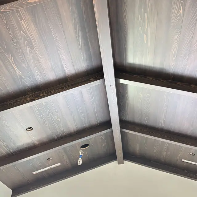 Vaulted tongue-and-groove wood ceiling with dark stained beams above white walls