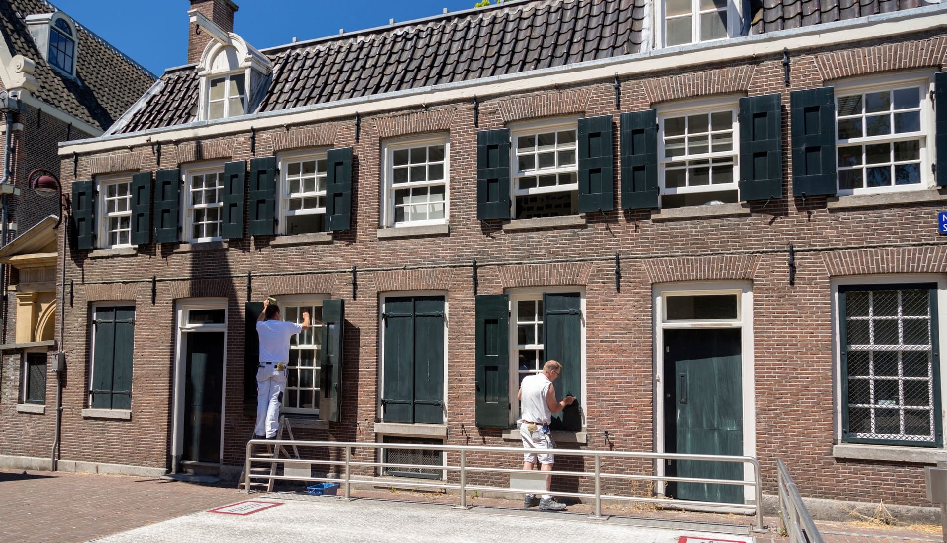 Two painters in white work uniforms repainting the window frames of a house facade