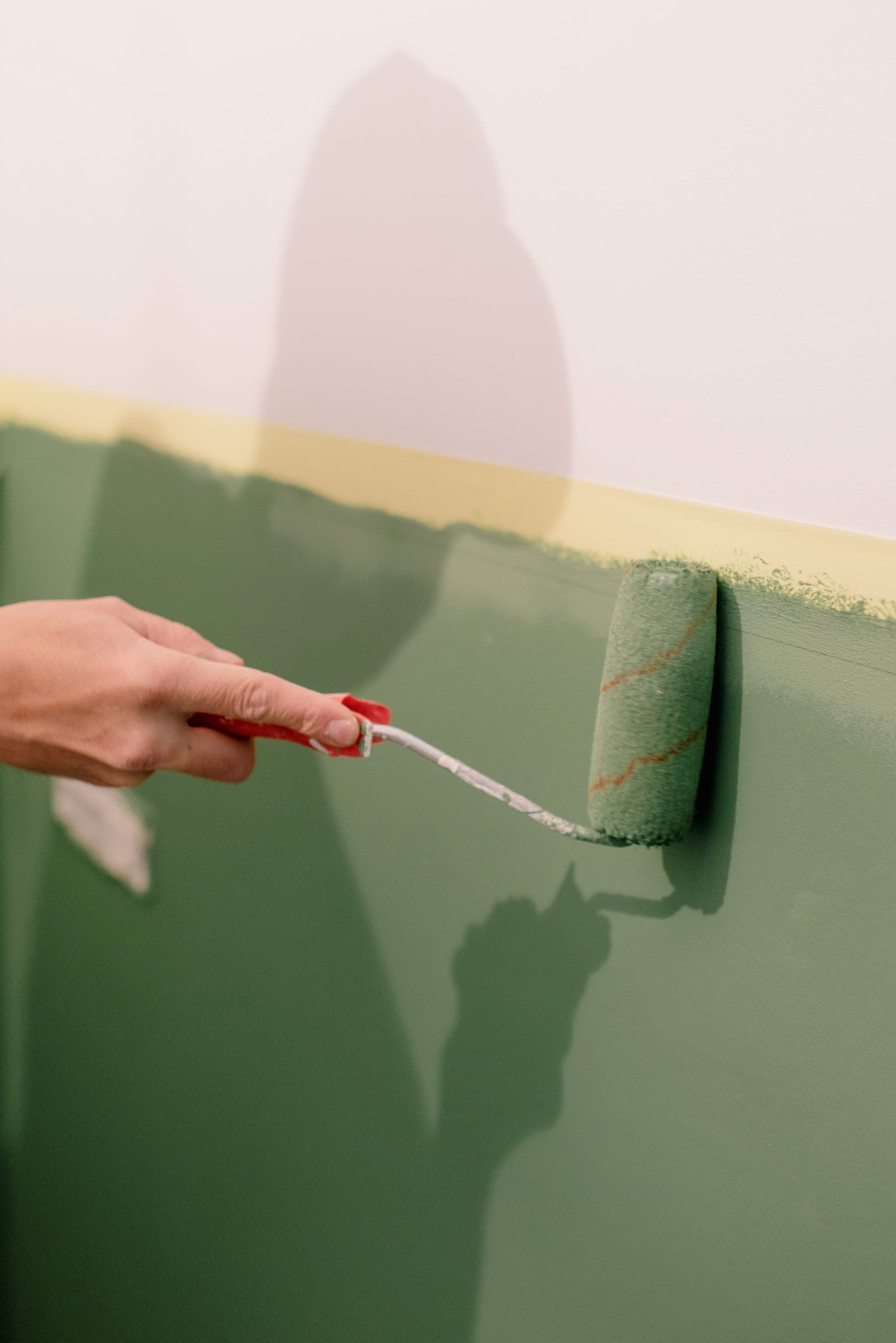 Roller applying fresh green paint to a wall above masked trim